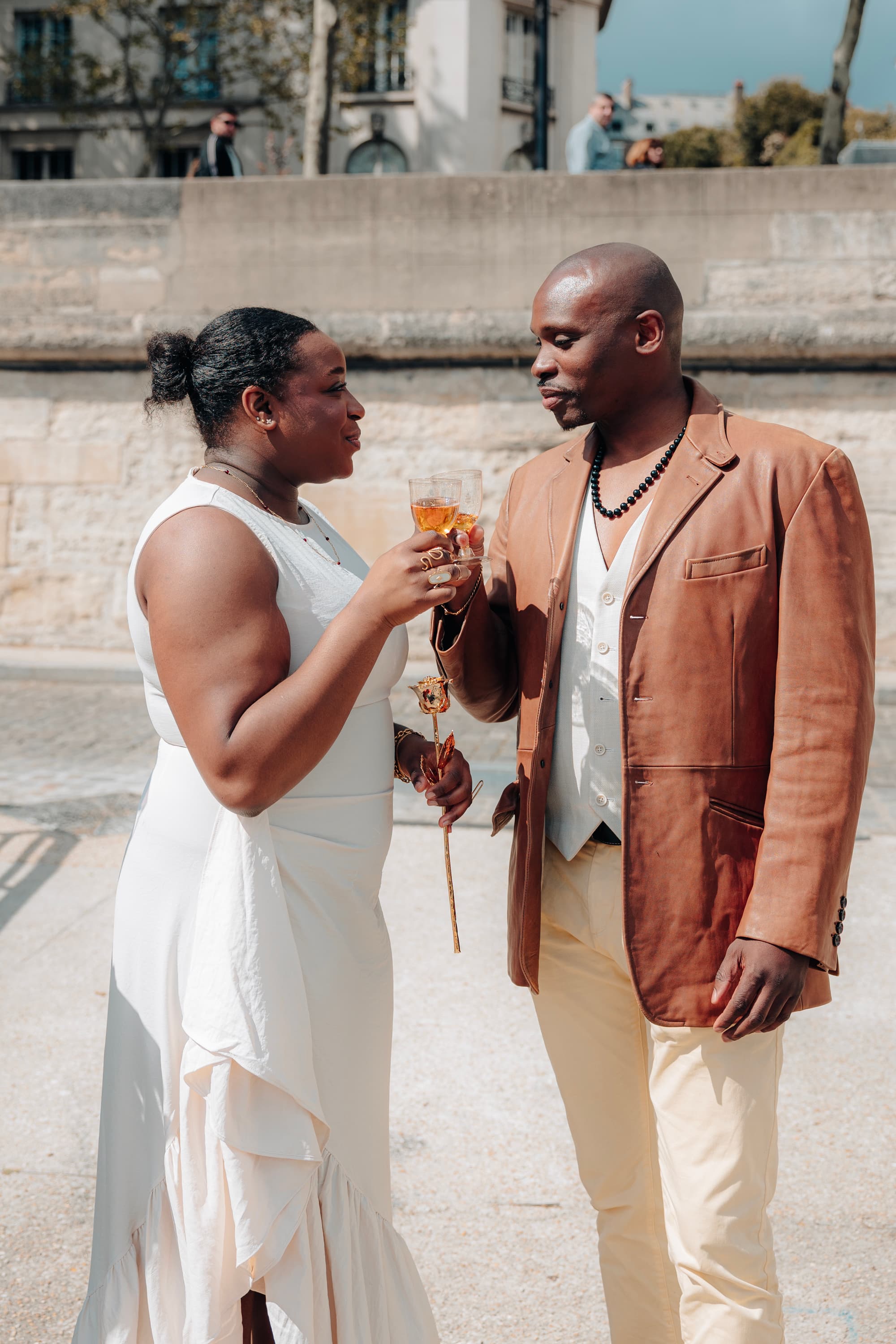 Thiya et Dahé se portent un toast, une rose dorée à la main, sur un quai de pierre claire