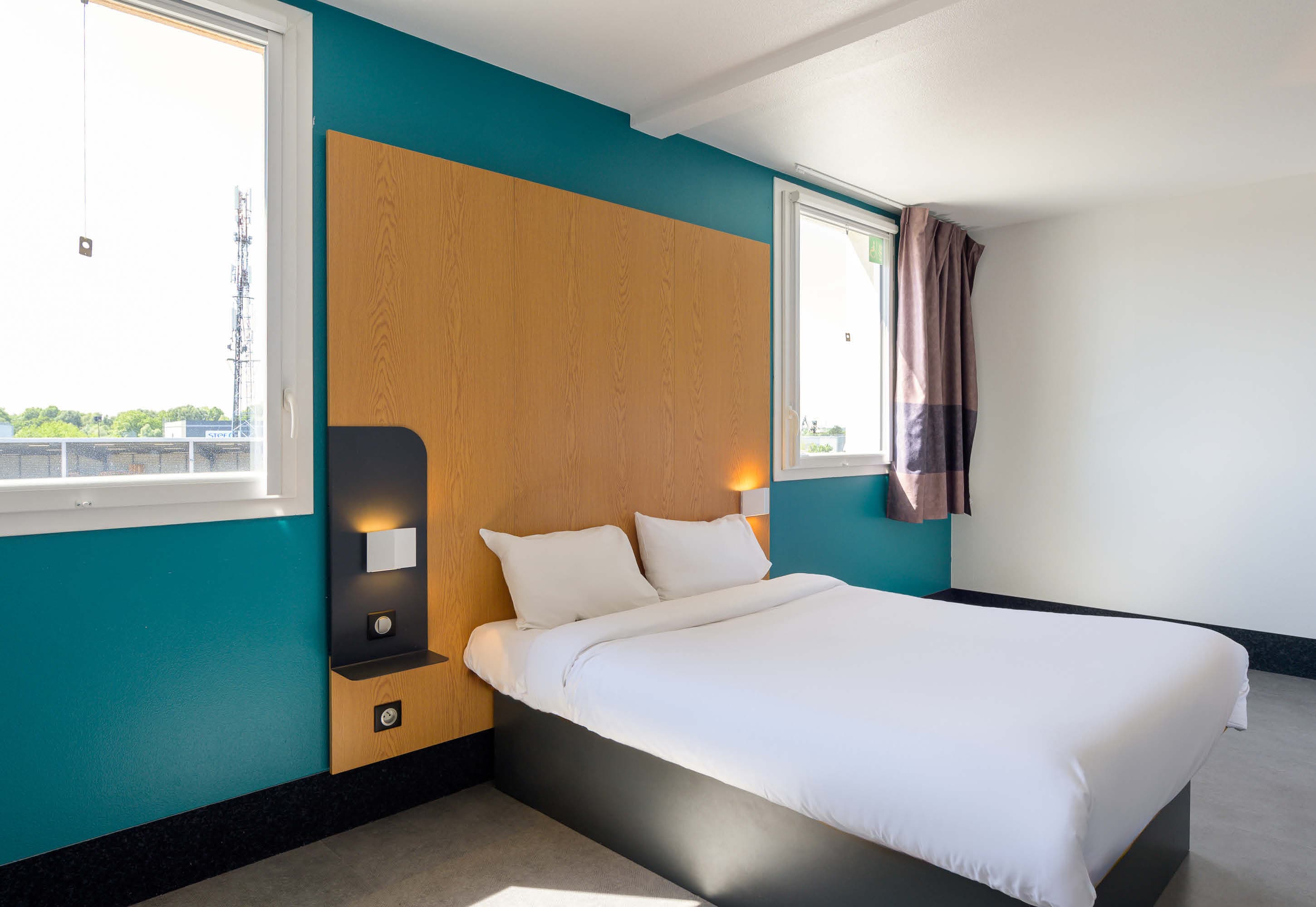Chambre du B&B Hôtel Carré Sénart, mur bleu canard et tête de lit en chêne